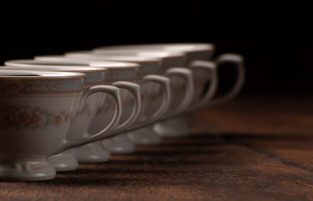 Tasses en porcelaine, belles tasses en porcelaine disposées géométriquement sur bois rustique, fond sombre, mise au point sélective.