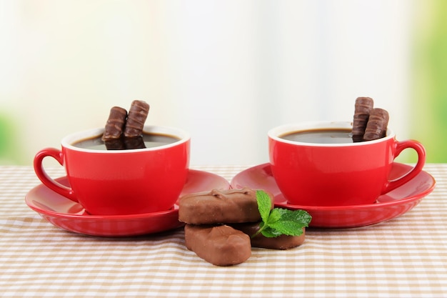 Tasses rouges de café fort et de barres de chocolat sur nappe sur fond clair