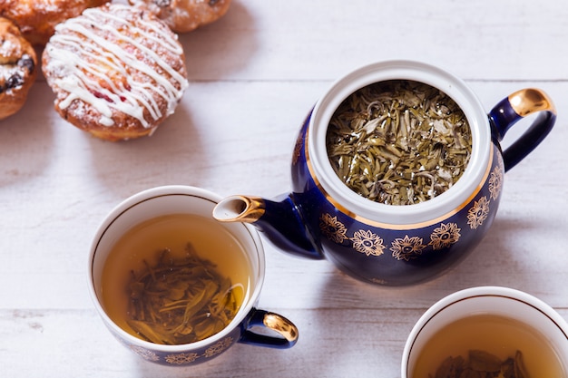 Tasses à thé, théière et muffins sur table en bois blanc, haut vue rapprochée