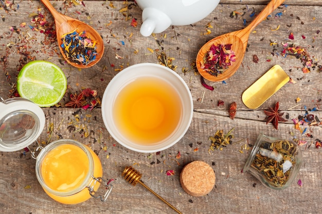 Tasses de tisane saine avec des fleurs de cannelle, de rose séchée et de camomille en cuillères sur du bois