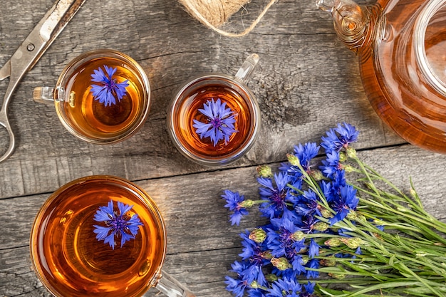 Tasses de tisane, théière transparente et fleurs de bleuets bleus