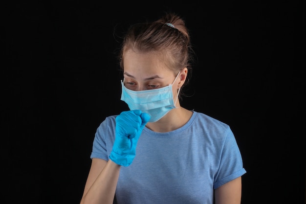 État de santé malade. Symptômes de la grippe, toux. Femme en gants médicaux, masque médical sur un mur noir