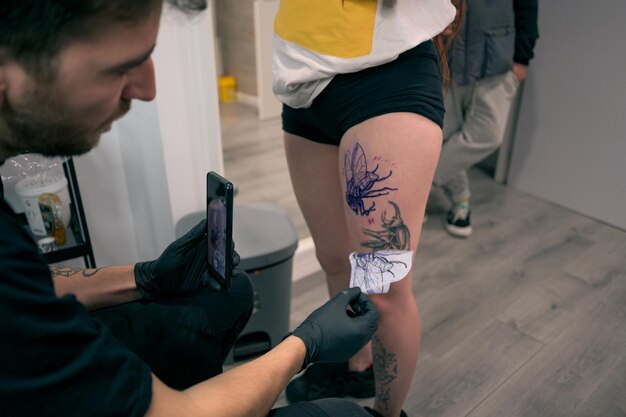 Un tatoueur applique un dessin détaillé de mouche sur la jambe d'un client en studio