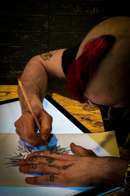 Photo tatoueur concevant un dessin de tatouage sur papier sur une tablette de dessin numérique dans son studio de tatouage
