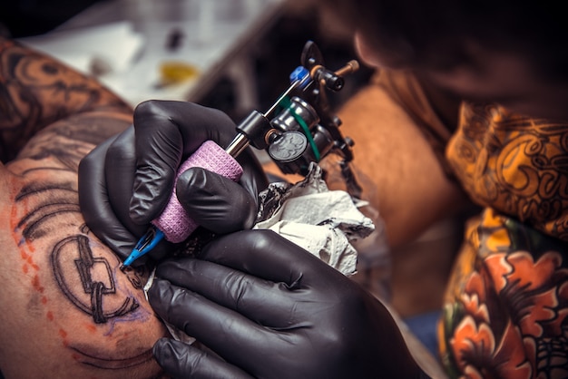 Un tatoueur crée un tatouage dans un studio de tatouage. / Homme portant des gants faisant un tatouage dans un salon de tatouage.