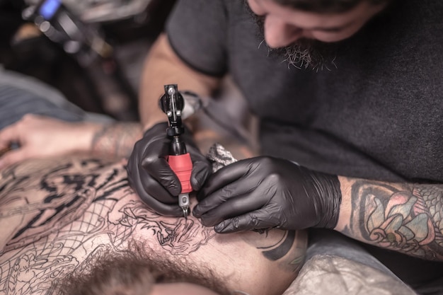 Un tatoueur démontre le processus de tatouage dans un salon de tatouage./Tattoo master posant dans le salon.