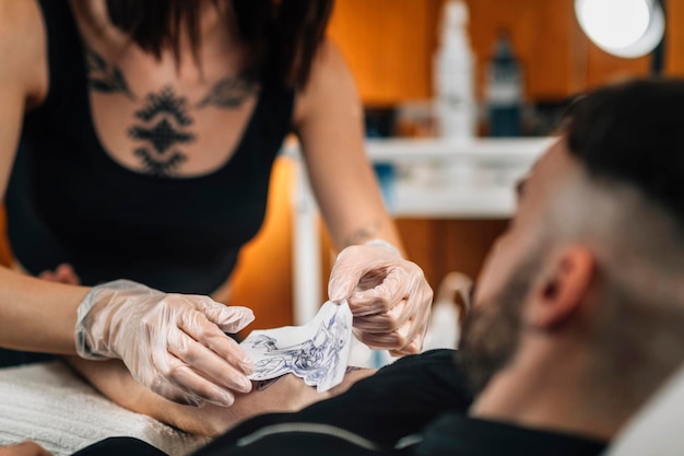 Tatoueur enlevant le pochoir d'un bras de clients