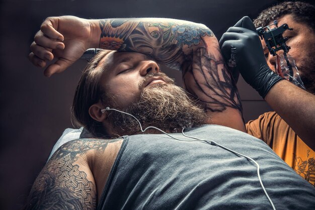 Tatoueur faisant du tatouage dans un studio de tatouage./Un tatoueur professionnel fait du tatouage dans un salon de tatouage.