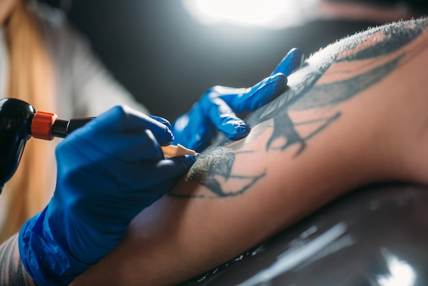 Un tatoueur fait un tatouage à la machine sur l'épaule masculine