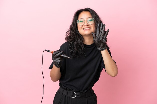 Tatoueur femme asiatique isolée sur fond rose comptant cinq avec les doigts