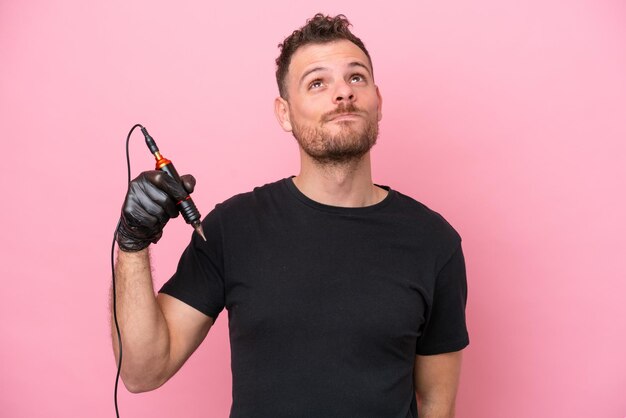 Tatoueur homme brésilien isolé sur fond rose et levant les yeux