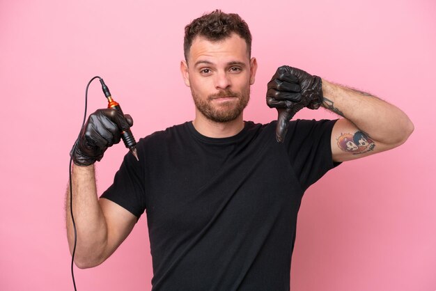 Tatoueur homme brésilien isolé sur fond rose montrant le pouce vers le bas avec une expression négative