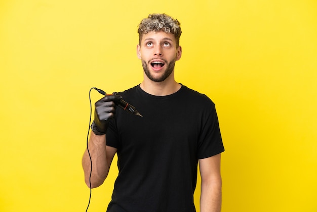 Tatoueur homme caucasien isolé sur fond jaune en levant et avec une expression surprise