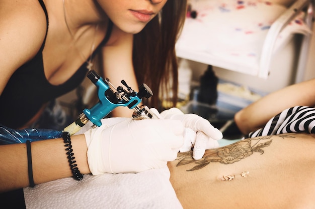 Tatoueur de jeune femme montrant le processus de fabrication d'un tatouage, conception de roses noires.