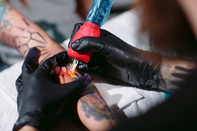 Un tatoueur professionnel fait un tatouage sur la main d'une jeune fille.