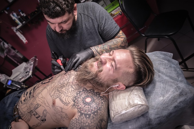 Tatoueur professionnel montrant le processus de fabrication d'un tatouage dans le salon./Le maître tatoueur fait un tatouage sur la peau dans le salon de tatouage.