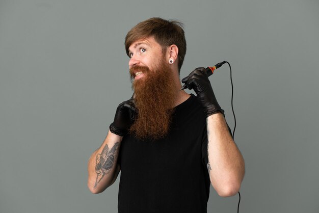 Tatoueur rousse homme isolé sur fond bleu en levant tout en souriant