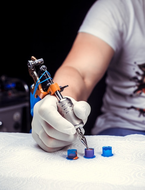 Un tatoueur tenant à la main une machine à tatouer.