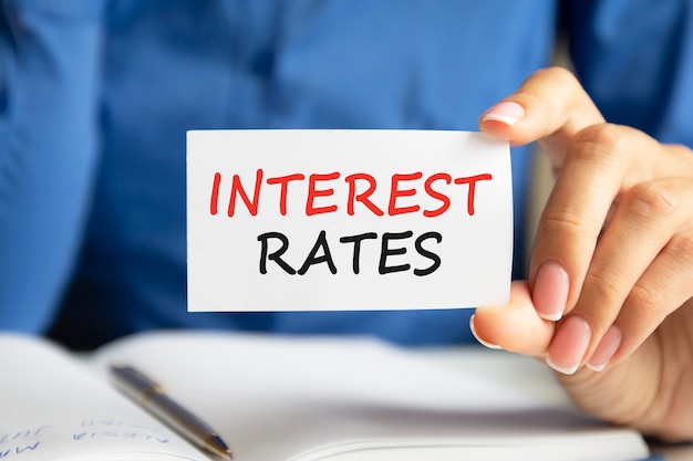 Les taux d'intérêt sont écrits sur une carte de visite blanche dans la main d'une femme. Fond bleu. Concept commercial et publicitaire