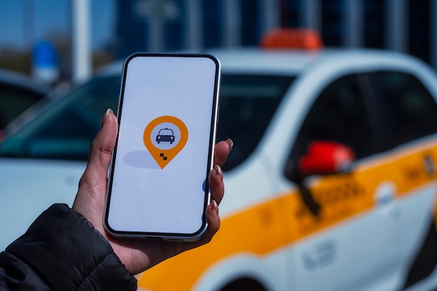 Taxi en ligne dans un smartphone. La fille tient le téléphone dans ses mains avec une application mobile à l'écran sur fond de voiture.