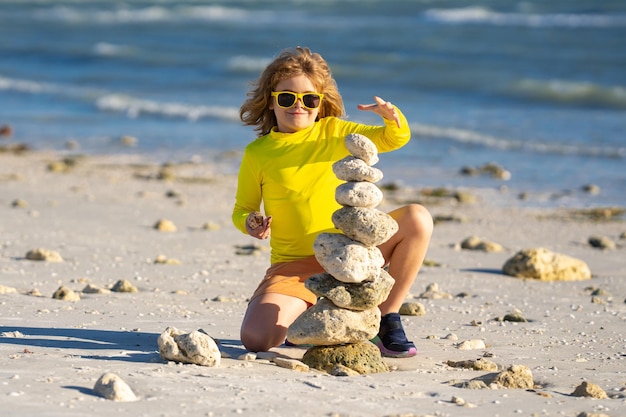 Été enfant méditation petit enfant jouer avec des pierres pyramidales équilibre sur le sable de la plage enfant avec