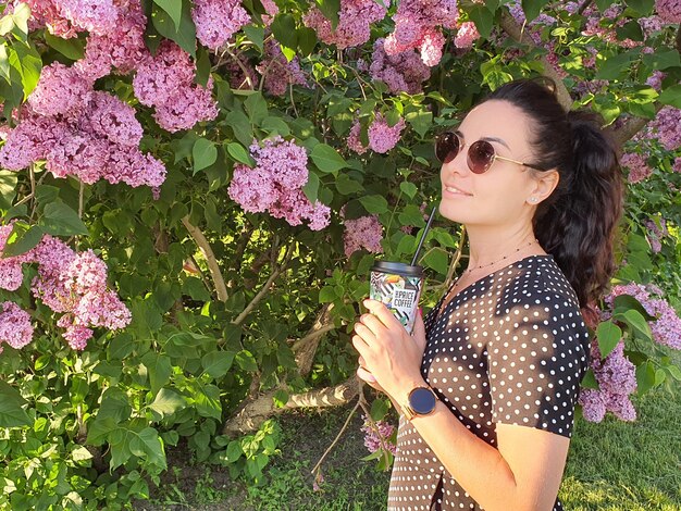 Été une fille à lunettes de soleil avec un verre dans ses mains buisson lilas