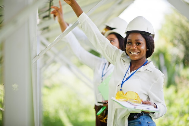 Un technicien afro-américain vérifie l'entretien des panneaux solaires Groupe de trois ingénieurs noirs réunis à la station solaire