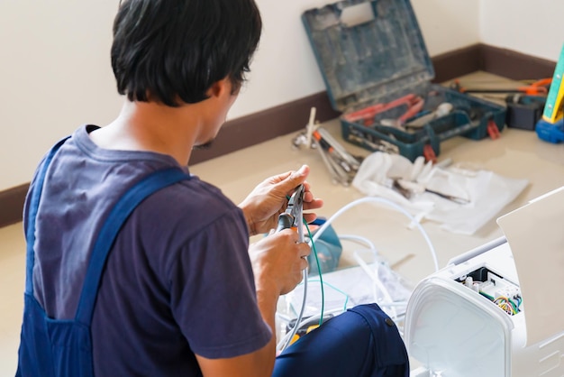 Technicien asiatique homme installant la climatisation dans la maison du client Jeune réparateur réparant l'unité de climatisation Concepts d'entretien et de réparation