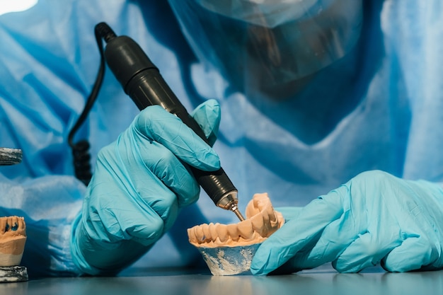 Un technicien dentaire masqué et ganté travaille sur une dent prothétique dans son laboratoire.