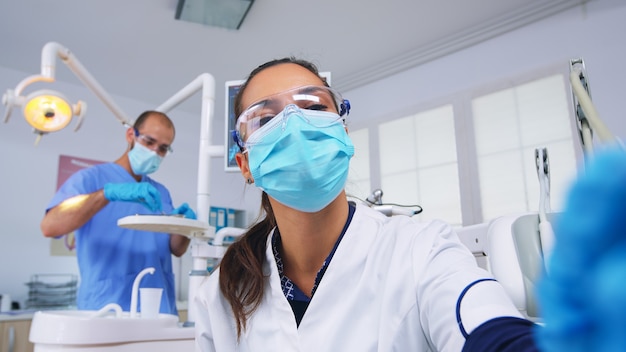 Technicien dentiste perçant la dent du patient dans une clinique dentaire, personne pov. Médecin avec masque tenant des outils examinant une femme souffrant de maux de dents assise sur une chaise stomatologique, infirmière préparant des outils pour la chirurgie