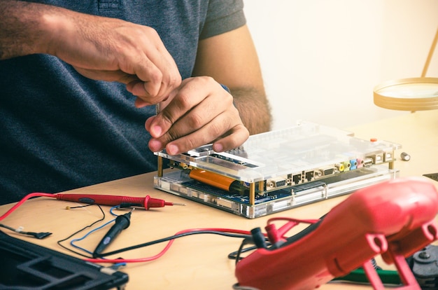 Technicien informatique fixant un ordinateur portable sur un bureau, avec des outils autour. Homme noir. Outils de travail.