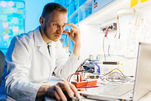 Technicien de laboratoire électronique portant une robe blanche utilise un ordinateur portable pour ses recherches