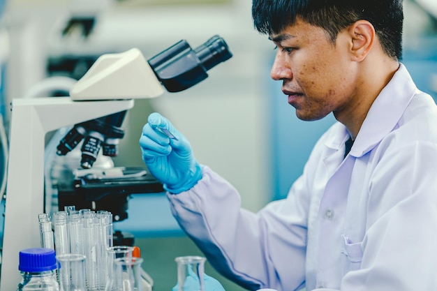 Un technicien de laboratoire d'homme asiatique portant des lunettes et des gants de protection est assis à côté d'un microscope en laboratoire