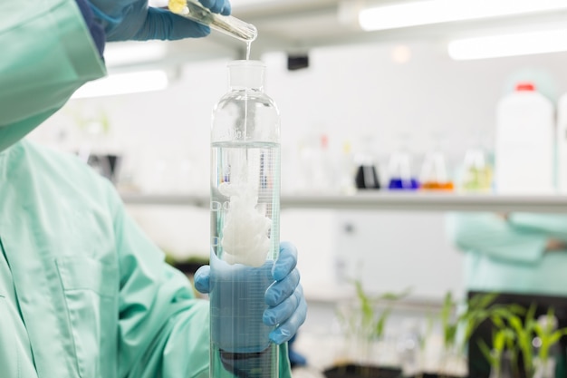 Le technicien de laboratoire verse du liquide dans un ballon haut du laboratoire.