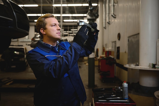 Technicien, mécanicien automobile, ingénieur automobile travaillant dans un atelier de réparation ou un garage de service automobile contre une voiture levée avec capot ouvert