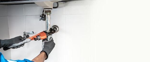 Technicien plombier utilisant une clé pour réparer une conduite d'eau sous l'évier