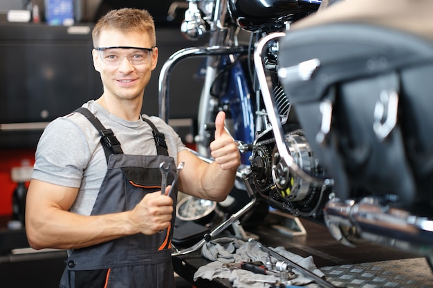 Photo un technicien en réparation de motos lève le pouce en se tenant debout dans l'atelier