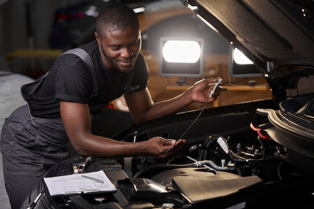 Technicien de service automobile professionnel africain en uniforme debout près du capot de la voiture