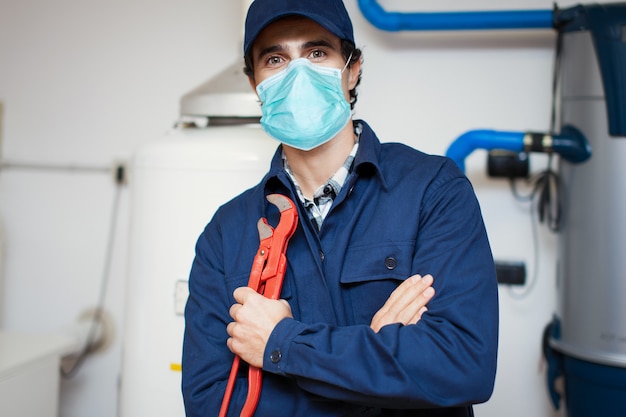 Photo technicien souriant réparant un chauffe-eau portant un masque, concept de coronavirus