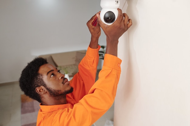 Technicien en uniforme orange installant la surveillance vidéo dans un immeuble de bureaux