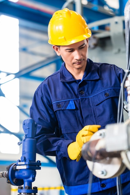 Technicien en usine asiatique à la maintenance de la machine travaillant avec une clé