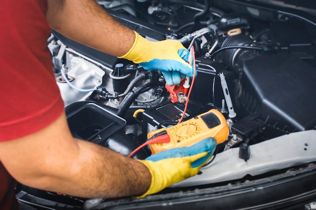 Technicien vérifiant la stabilité de la tension continue de la batterie de la voiture avec une sonde multimètre numérique