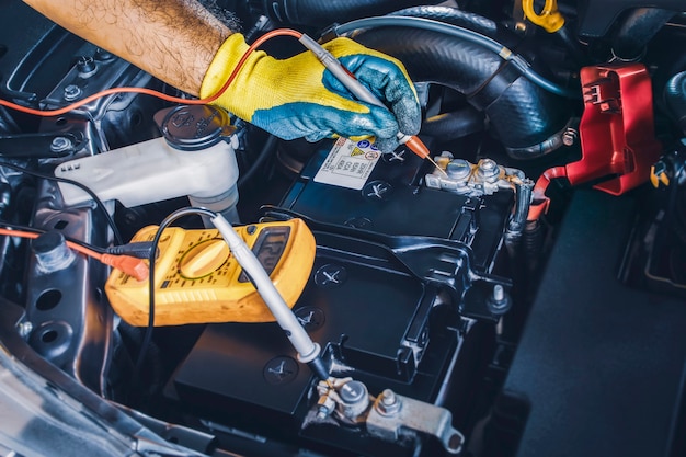 Technicien vérifiant la stabilité de la tension continue de la batterie de la voiture avec une sonde multimètre numérique