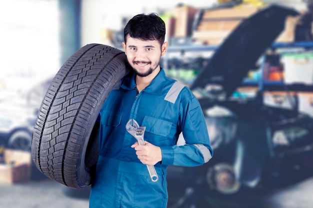 Technicien avec un vêtement de travail bleu debout tenant une clé et un pneu