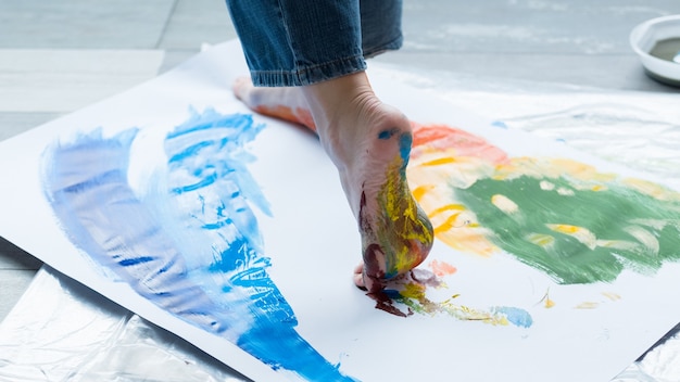 Technique de peinture au pied. Photo recadrée d'un artiste marchant sur papier, créant des œuvres d'art abstraites colorées.
