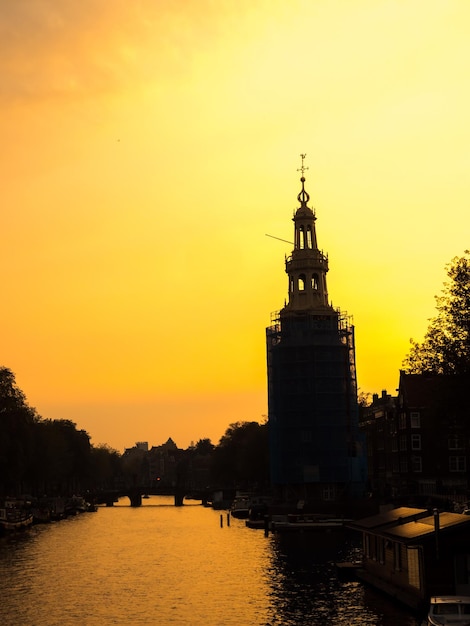 Technique de la silhouette de la tour de l'horloge le long du canal à Amsterdam sous un ciel doré en soirée