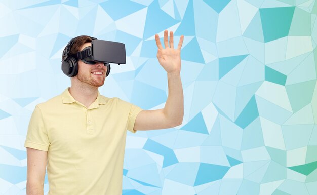 Technologie 3d, réalité virtuelle, concept de divertissement et de personnes - jeune homme heureux avec un casque de réalité virtuelle ou des lunettes 3d jouant à un jeu sur fond low poly