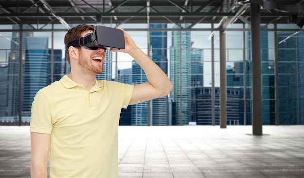 Technologie 3d, réalité virtuelle, concept de divertissement et de personnes - jeune homme heureux avec un casque de réalité virtuelle ou des lunettes 3d jouant à un jeu sur une salle vide industrielle et un arrière-plan panoramique de la ville