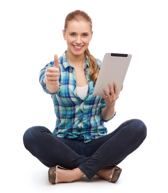 technologie et concept internet - jeune femme souriante dans des vêtements décontractés assise sur le sol avec un ordinateur tablette et montrant les pouces vers le haut