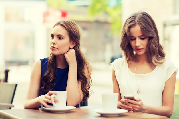 technologie, dépendance à Internet, mode de vie, amitié et concept de personnes - jeunes femmes ou adolescentes avec smartphones et tasses à café au café en plein air